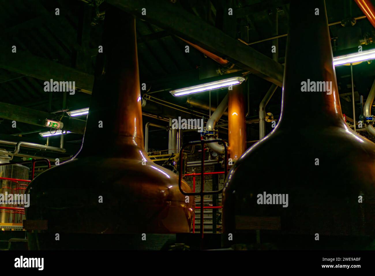 Distillatori industriali in rame e serbatoi di fermentazione in un ambiente buio con illuminazione ambientale. Foto Stock