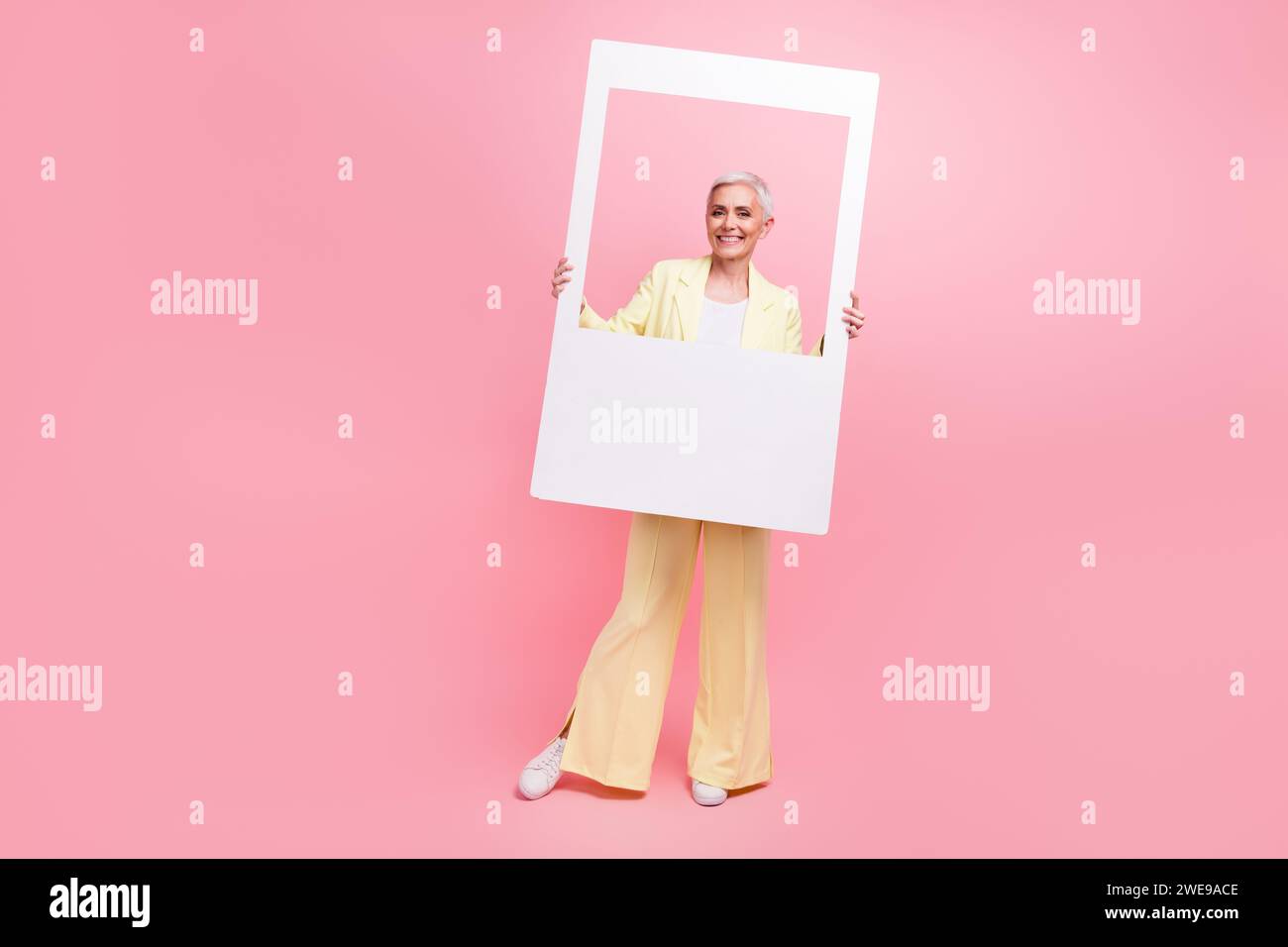 Foto a grandezza naturale di una donna di buon umore vestita in costume giallo che posa in una cornice fotografica per scattare istantanee immagini isolate su sfondo rosa Foto Stock