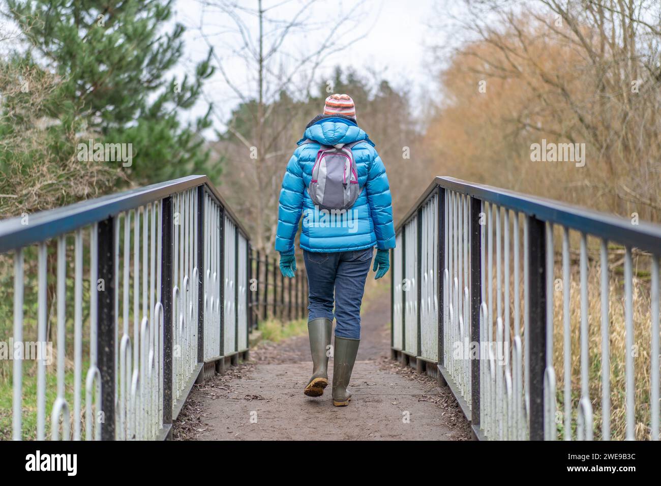 Vista posteriore di una donna che cammina su un ponte in una fredda giornata invernale. Donna che indossa un cappotto caldo, guanti e cappello. Foto Stock