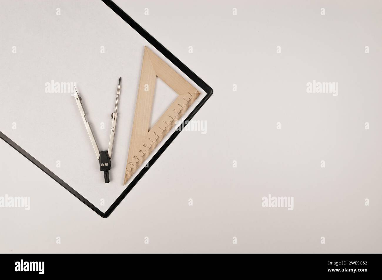 Vista dall'alto degli Appunti neri, bianco, righello a triangolo e bussola su sfondo bianco. Disegno di architettura, layout piatto, spazio di copia. Foto Stock