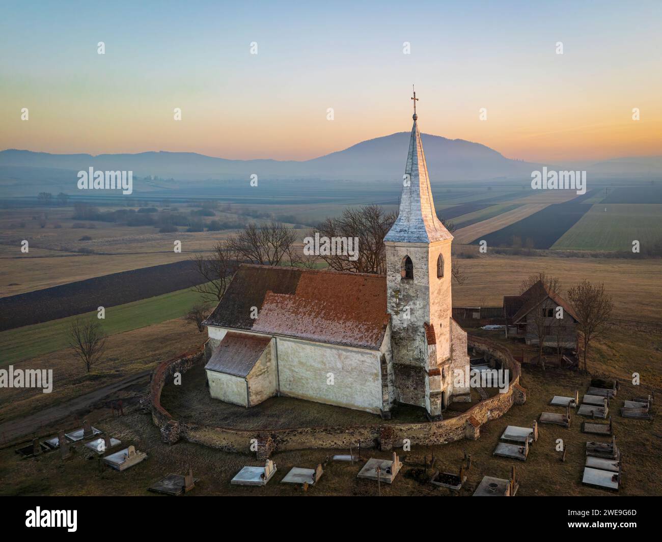 La vecchia chiesa di Delnita durante un tramonto spettacolare. Foto aerea scattata il 29 dicembre 2023 a Delnita, contea di Harghita, Transilvania, Romania. Foto Stock