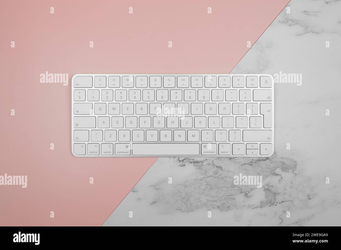 Vista dall'alto della tastiera bianca su sfondo in marmo rosa e bianco. Moderno spazio per fotocopie e ufficio. Foto Stock