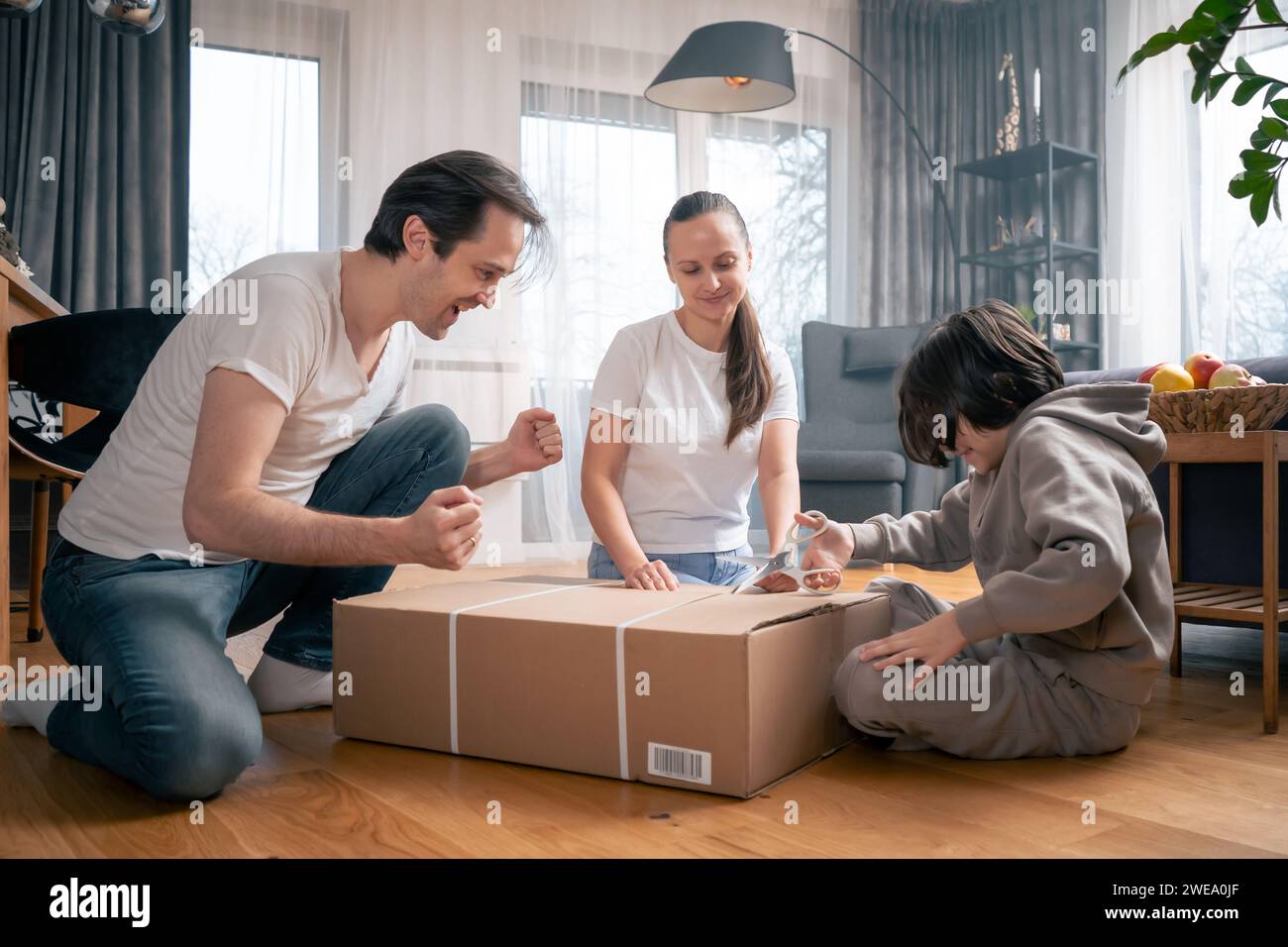 Una famiglia felice è impaziente di disimballare una grande scatola di cartone con un ordine da un negozio online che è stato consegnato a casa. Foto Stock