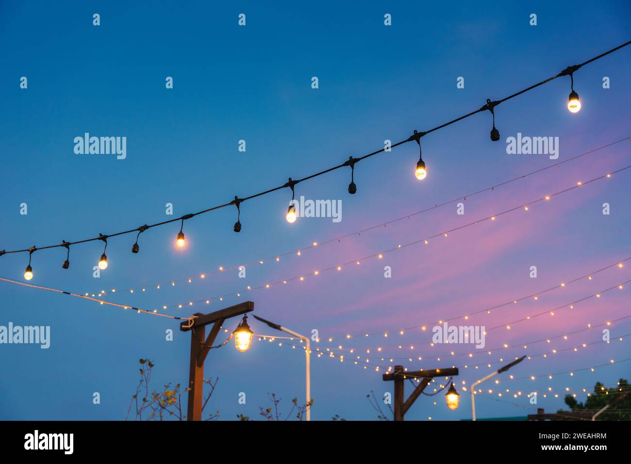 Lampadina retrò che si illumina con un cordoncino appeso decorativo al cortile per festeggiamenti al tramonto Foto Stock
