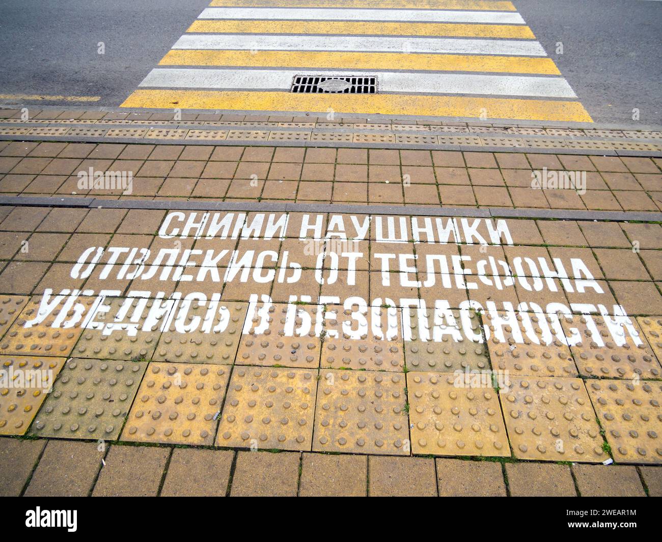 L'iscrizione di fronte all'attraversamento pedonale "togliete le cuffie, distogliete gli occhi dal telefono, assicuratevi di essere al sicuro" Foto Stock