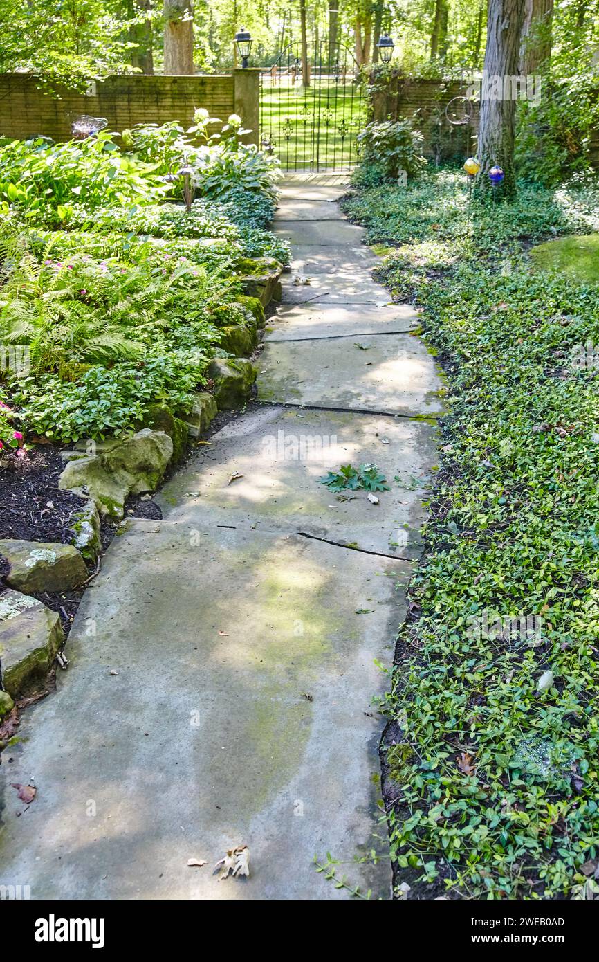 Sentiero con giardino sereno con cancello in ferro battuto e vegetazione lussureggiante Foto Stock