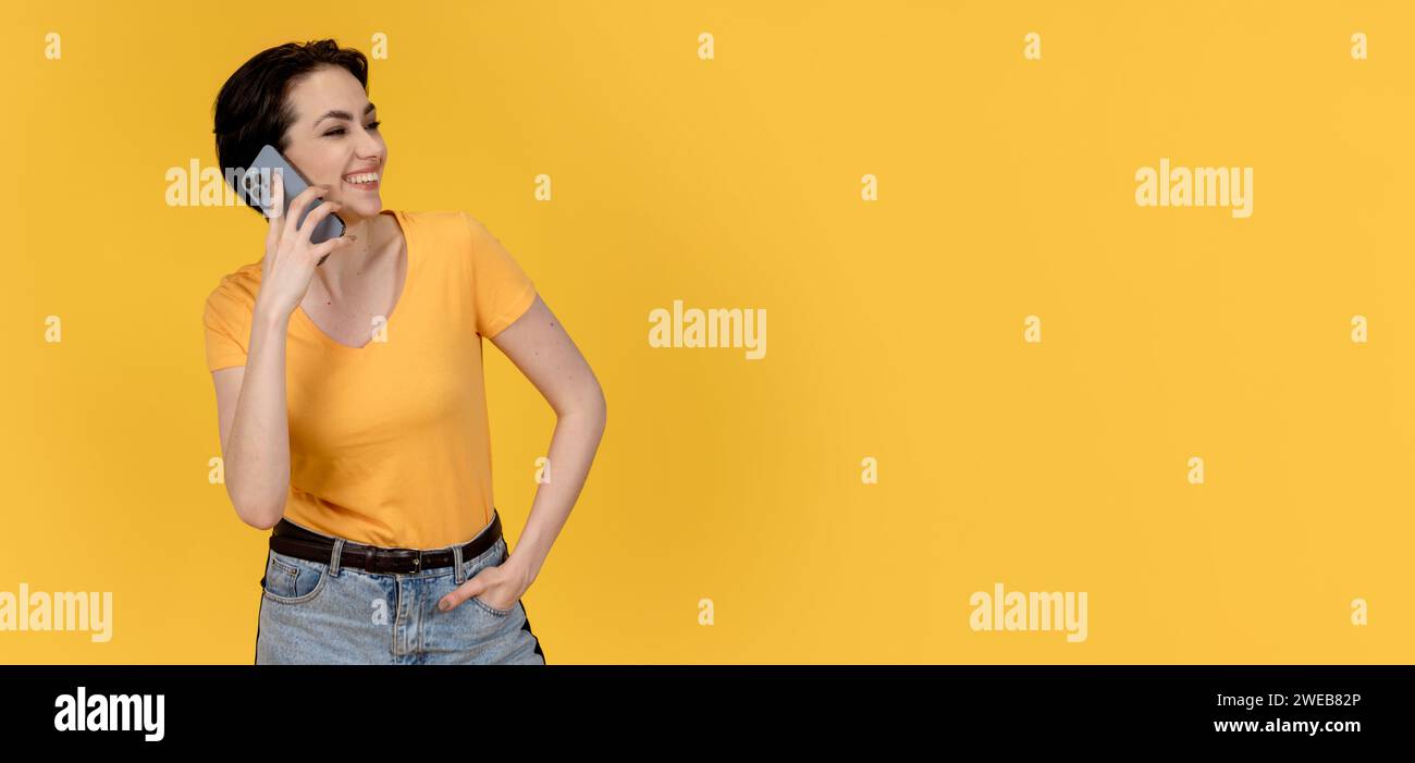 Happy Woman con t-shirt gialla e jeans che utilizza un telefono cellulare su sfondo giallo Copia spazio Foto Stock