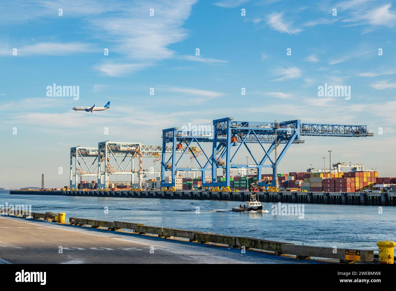 Boston, ma, US-8 dicembre 2023: Grandi gru di carico in porto pronte a caricare container su navi con aerei commerciali che volano sopra di loro. Foto Stock