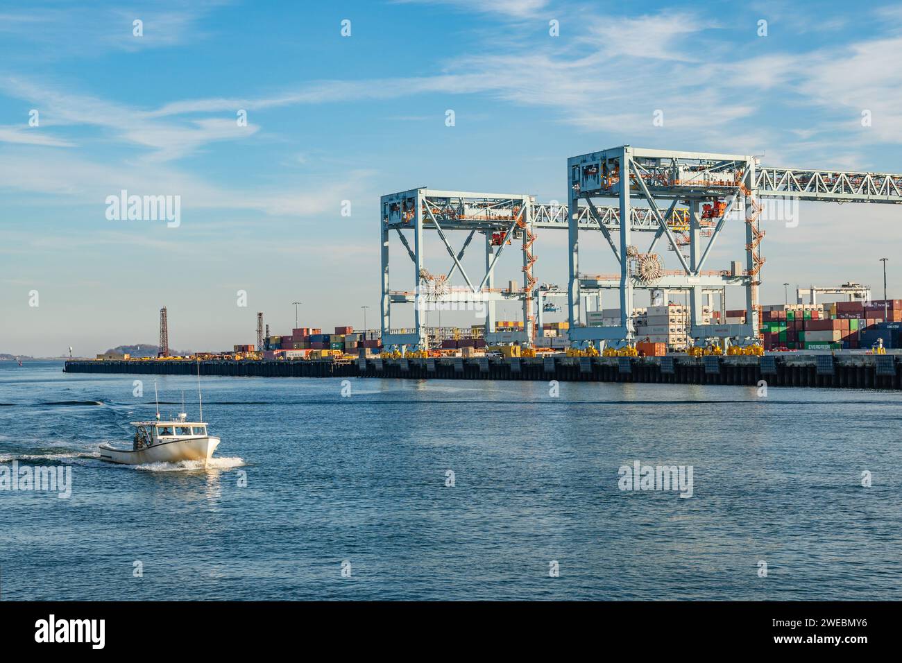 Boston, ma, US-8 dicembre 2023: Grandi gru di carico in porto pronte a caricare container su navi con aerei commerciali che volano sopra di loro. Foto Stock