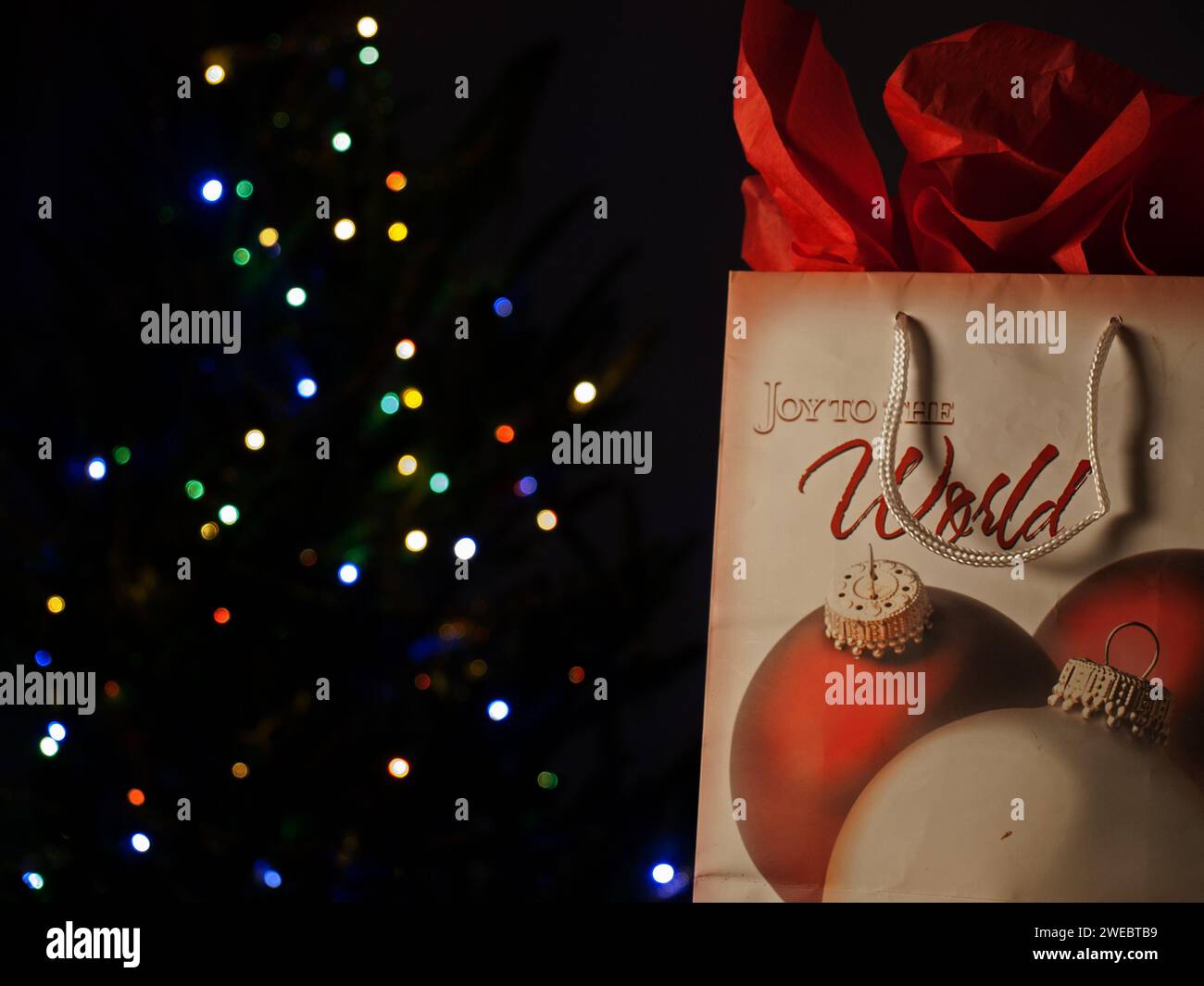 Borsa di Natale con un regalo e un albero illuminato dietro. Regali natalizi. Foto Stock