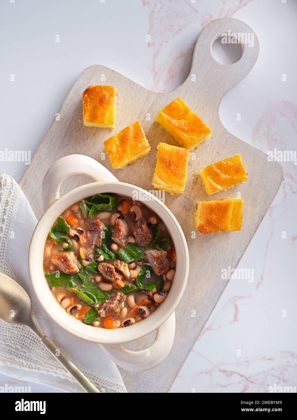 Piatto tipico DEGLI STATI UNITI con piselli dagli occhi neri, verdure al collardo, pane di maiale e mais su un tagliere bianco; spazio per copiare Foto Stock