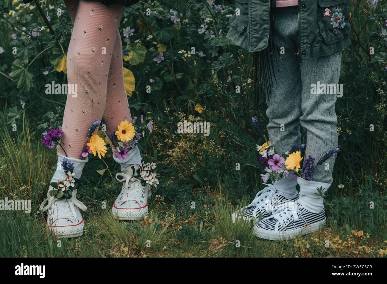 Personaggi stravaganti - sorelle che si tengono per mano e che si divertono con fiori luminosi nei loro panni - che piantano bambini nella natura per crescere. Foto Stock