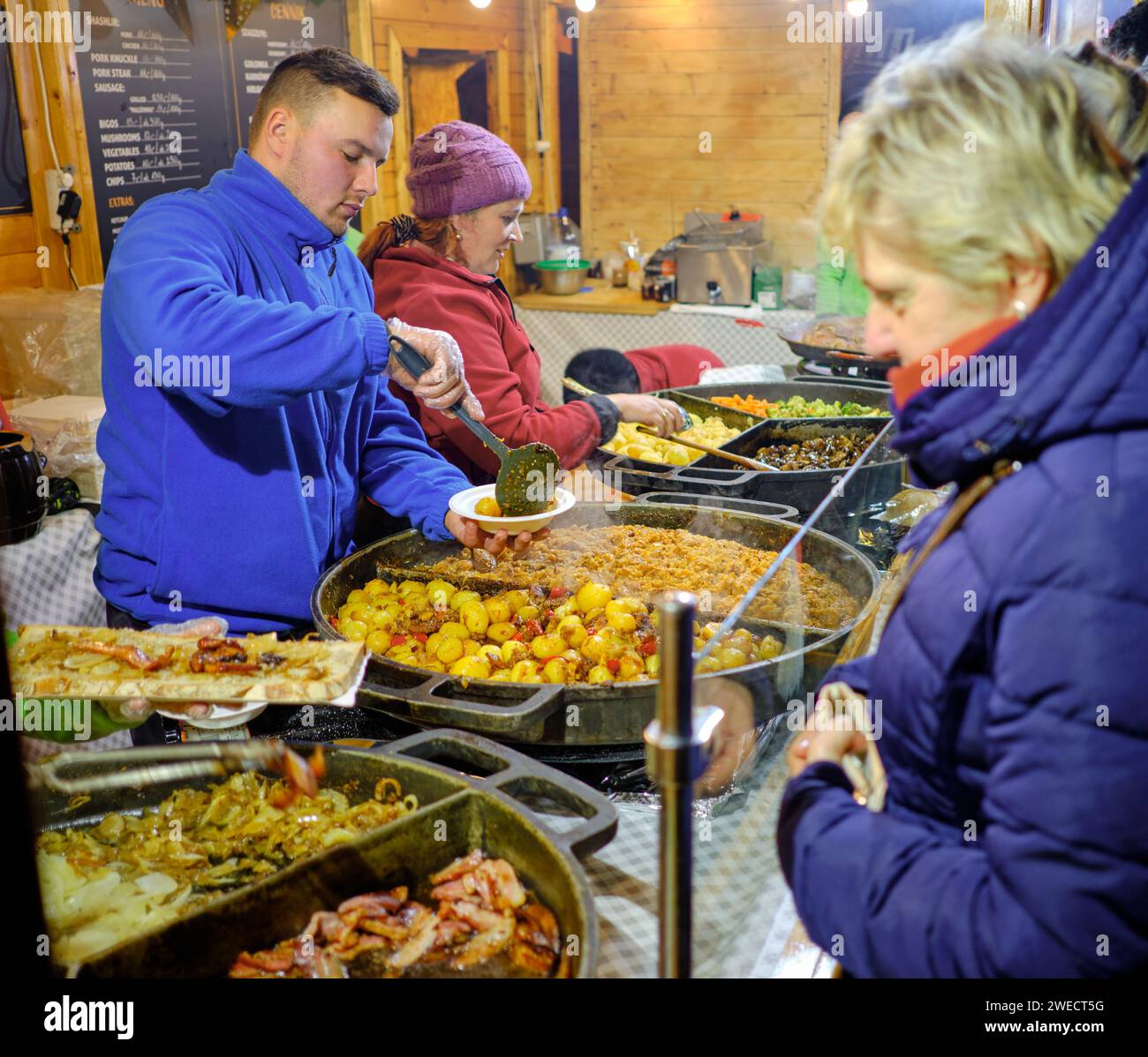 Wroclaw, Poland, cameriere di cibo maschile che gusta piatti tradizionali polacchi presso le bancarelle di cibo durante il mercato dell'Avvento di notte Foto Stock