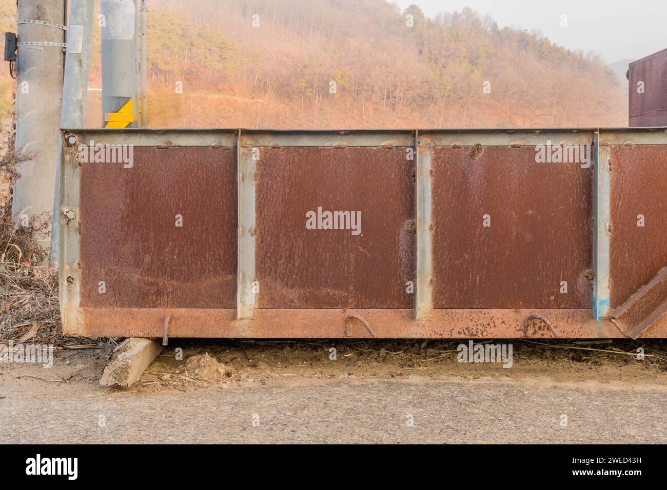 Un vecchio letto di ferro per camion sul lato della strada di campagna nella mattinata nebbiosa con campo e montagna sullo sfondo Foto Stock