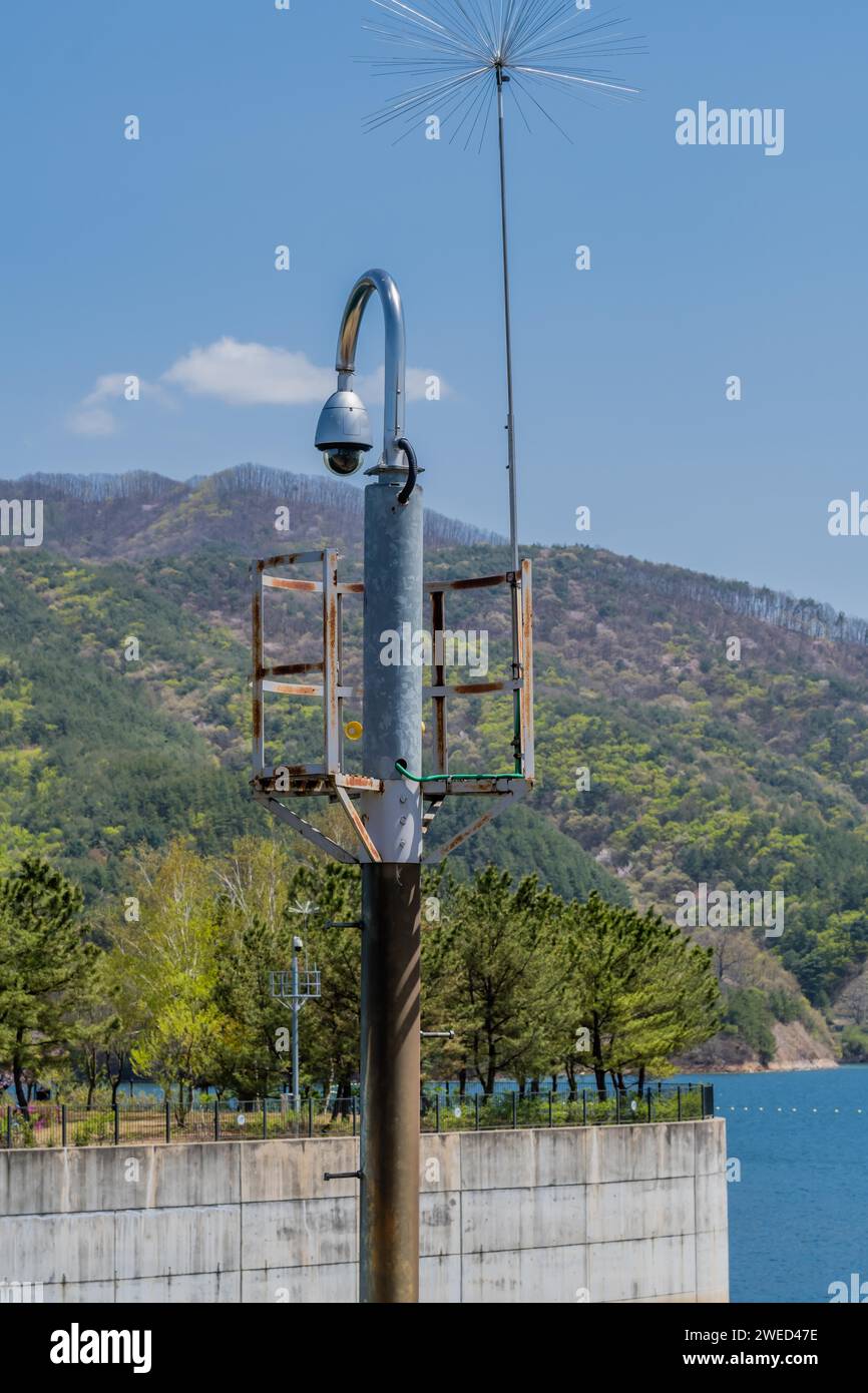 Telecamera rotonda a circuito chiuso su palo curvo con lago e montagna sotto il cielo blu sullo sfondo Foto Stock