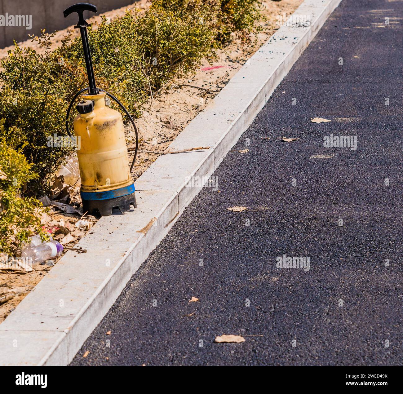 Flacone spray industriale in plastica situato sul marciapiede del parcheggio con pavimentazione in asfalto nero e una fila di cespugli verdi Foto Stock