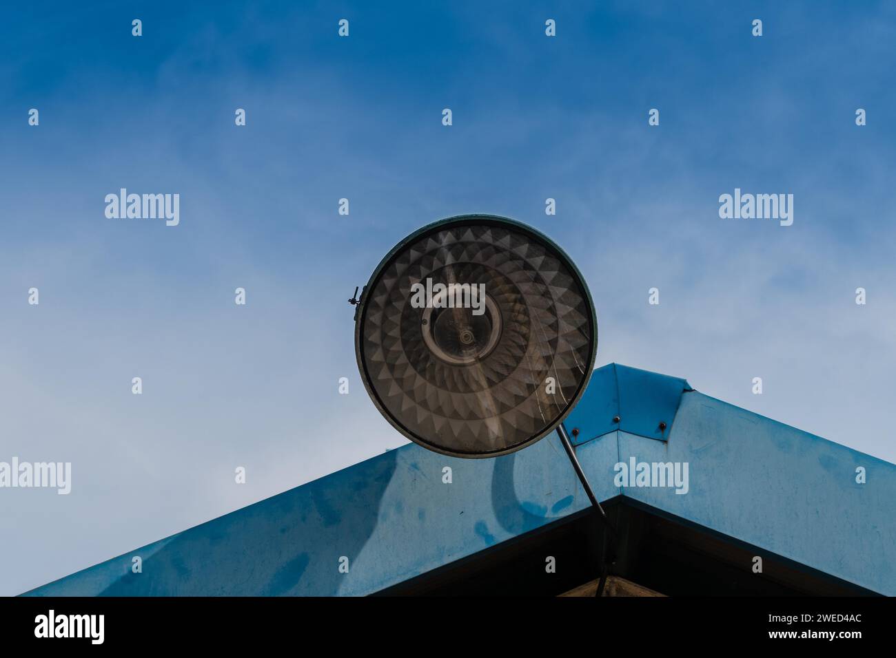 Grande illuminazione stradale con un paralume in metallo montato sul tetto di un edificio in metallo con cielo blu sullo sfondo Foto Stock