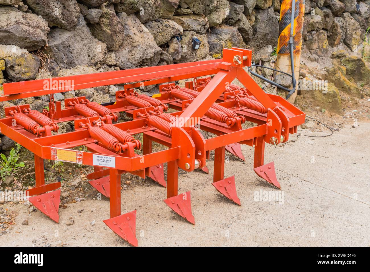 Aratro arancione brillante appoggiato contro il muro di pietra a Jeju, Corea del Sud Foto Stock