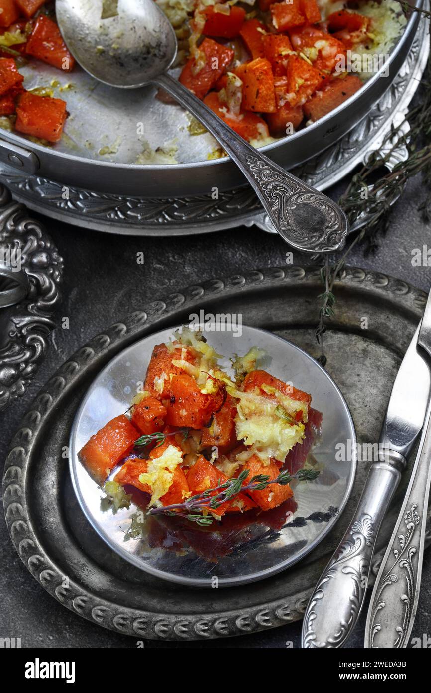 Zucca al forno con aglio, spezie e formaggio su sfondo nero Foto Stock