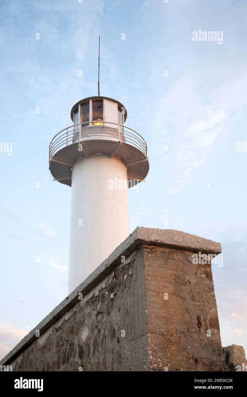 La torre bianca del faro e le pareti in pietra sono sotto il cielo blu in una foto verticale diurna. Porto di Varna, Bulgaria Foto Stock