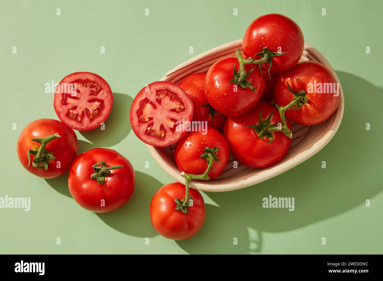 Un cestino pieno di pomodori rossi e pomodori tagliati a metà. Il pomodoro (Solanum lycopersicum) è una fonte di nutrienti come potassio, vitamina A, vi Foto Stock