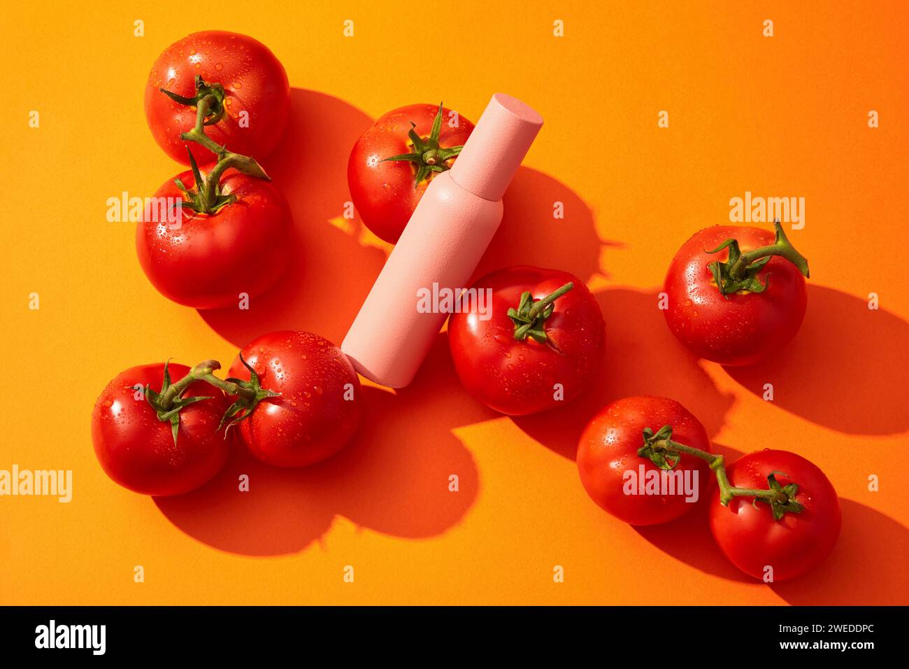 Il biberon rosa per la cura della pelle senza etichetta è decorato con molti pomodori. Il pomodoro (Solanum lycopersicum) contiene licopene che protegge dall'innocue Foto Stock
