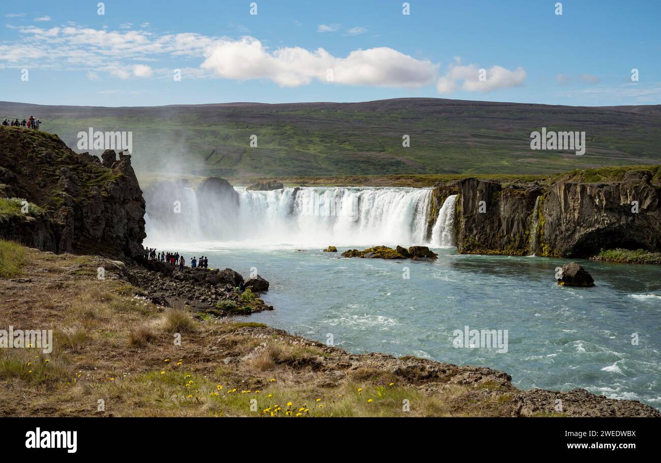 I piccoli turisti ammirano la maestosa cascata di Godafoss sul fiume Skjalfandafljot nel nord dell'Islanda, con una splendida collina verde sullo sfondo Foto Stock