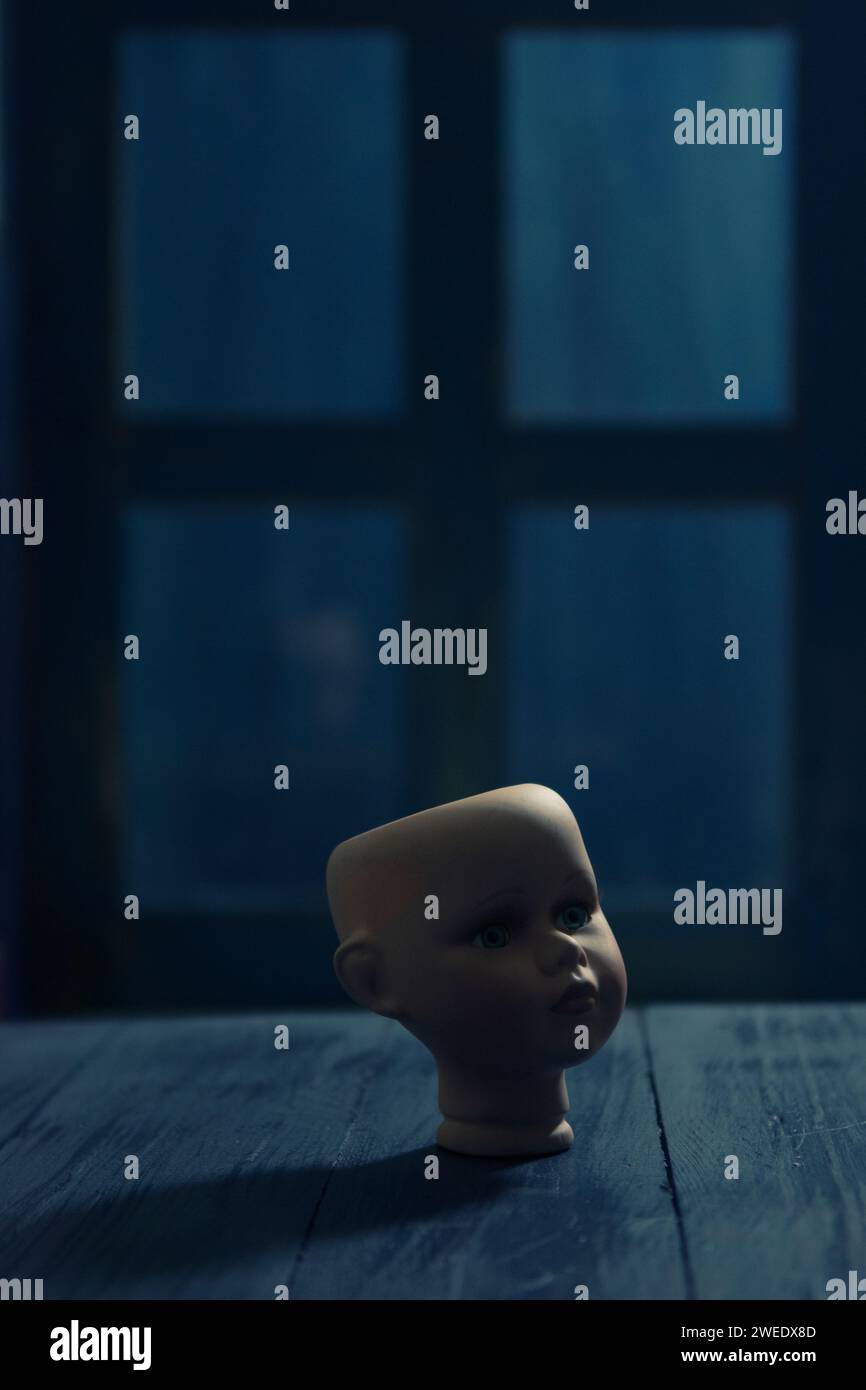 La testa della bambola inquietante vicino alla finestra di notte Foto Stock