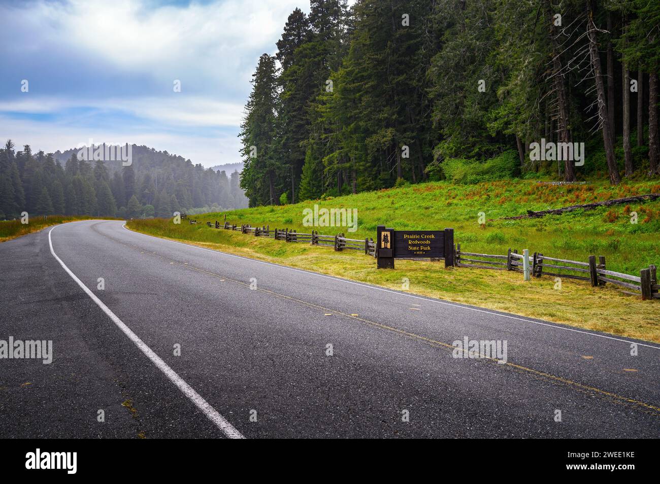 Strada curva che conduce al Prairie Creek Redwoods State Park con cartello di benvenuto Foto Stock