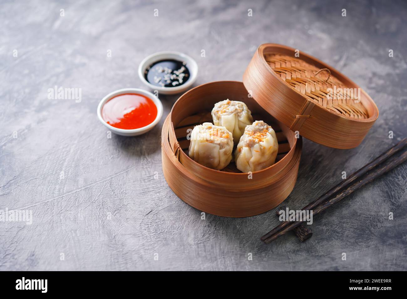 Gnocchi cinesi al vapore o Dim Sum in una vaporiera di bambù su sfondo astratto scuro Foto Stock