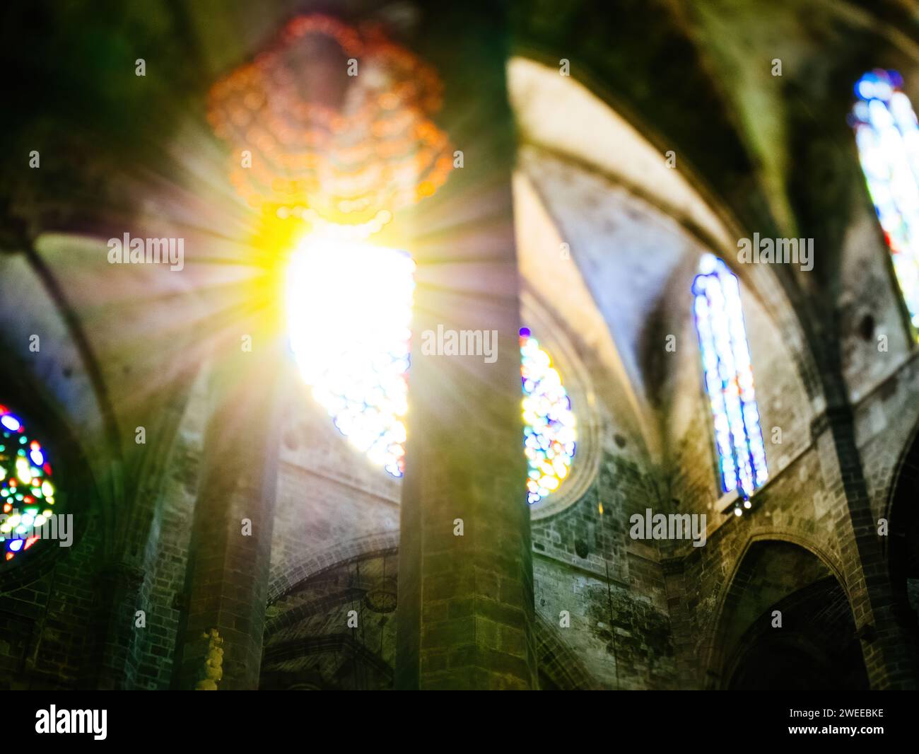 La calda luce del sole filtra attraverso una vetrata colorata della Catedral-Basilica de Santa Maria a Palma di Maiorca, Spagna, proiettando riflessi colorati, catturati con una lente inclinabile. Foto Stock