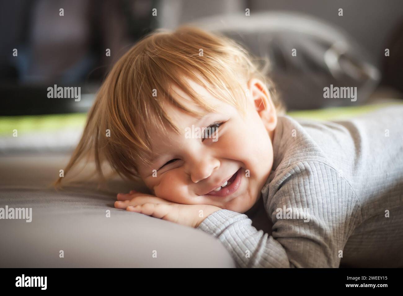 Ritratto di un bambino sorridente che si appoggia sul divano e guarda la fotocamera. Concetto di gioia e felicità. Amore ed emozione familiare Foto Stock