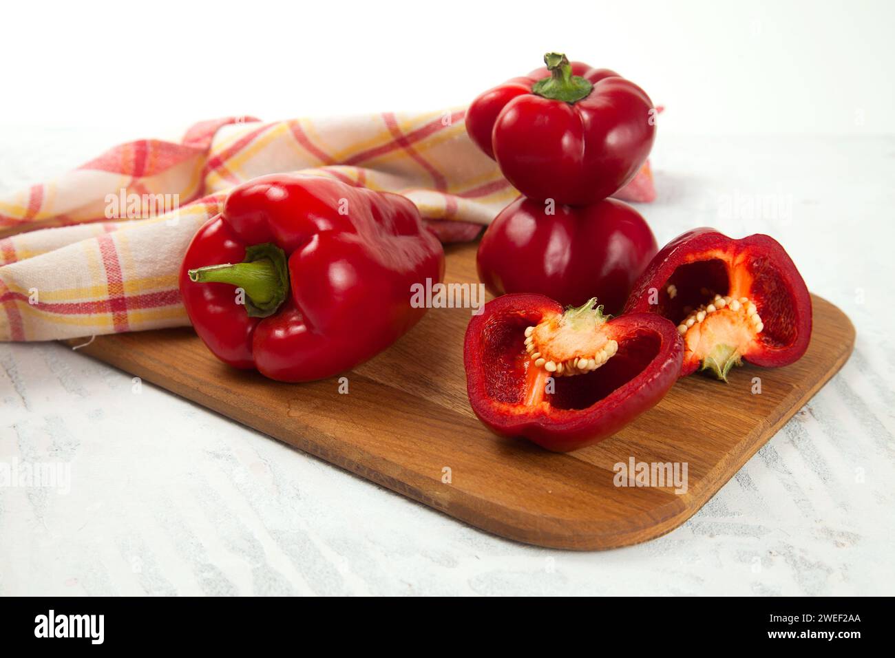 Tagliere con diverse tagliere interi e metà di peperone rosso (capsicum) noto come peperone dolce, paprika e asciugamano da cucina rosso su ba di legno bianco Foto Stock