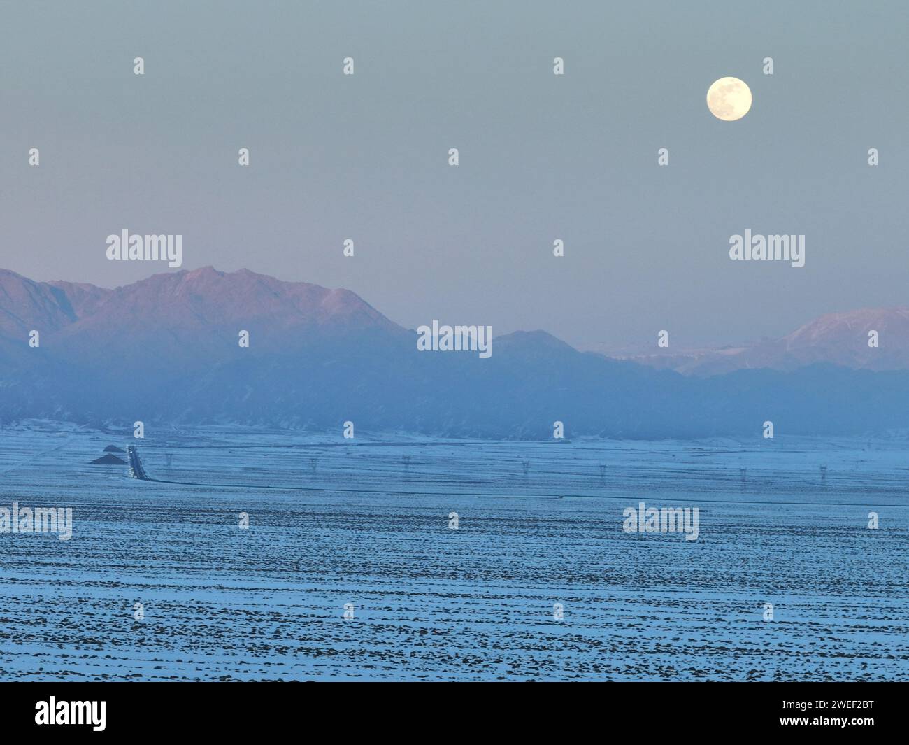 HAMI, CINA - 25 GENNAIO 2024 - Una luna luminosa sorge sui monti Tianshan orientali a Hami, provincia dello Xinjiang, Cina, 25 gennaio 2024. Il primo pieno Foto Stock