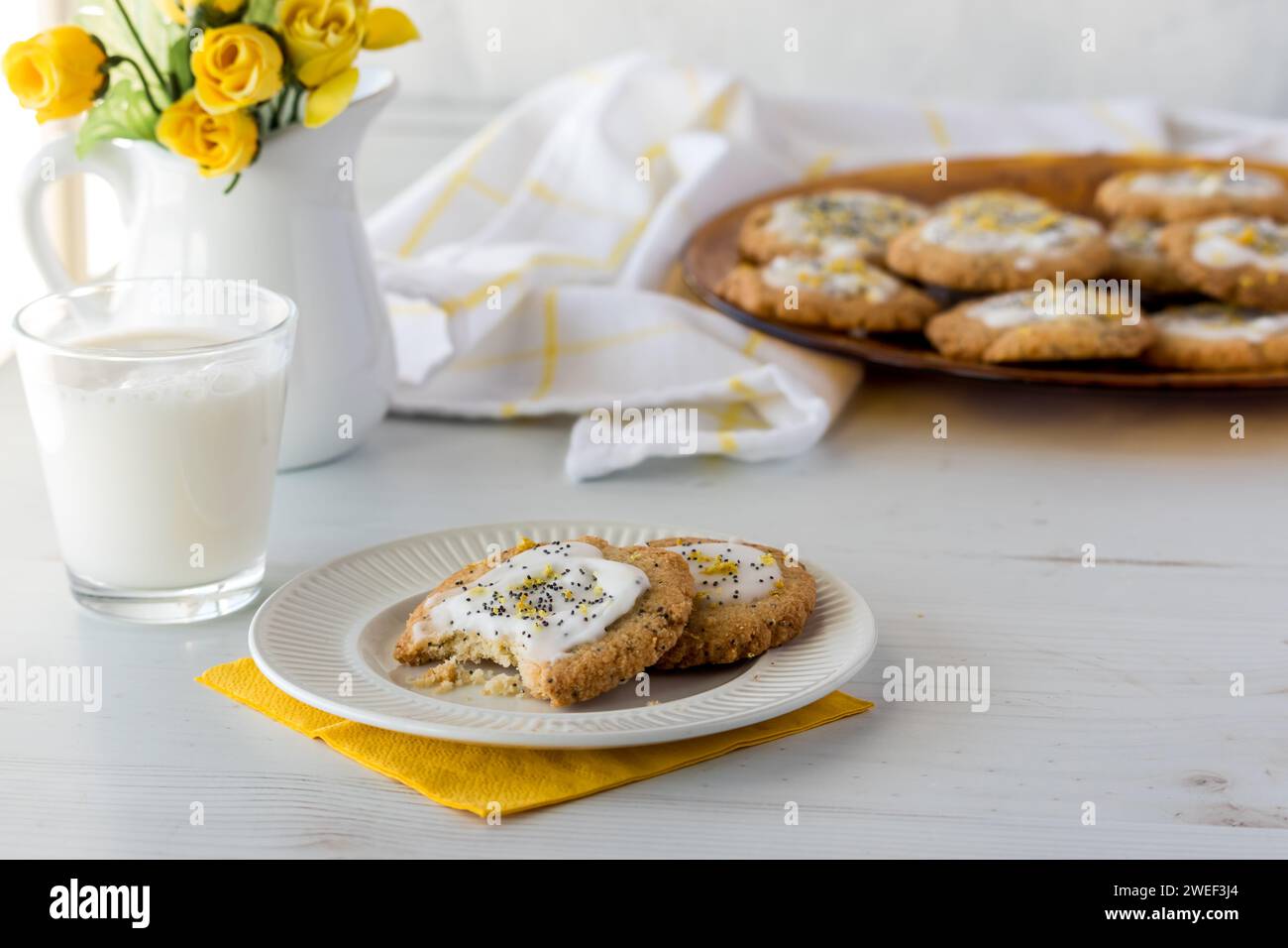 Biscotti keto al limone con semi di pappe serviti con latte e un vassoio di altri ingredienti dietro di te. Foto Stock