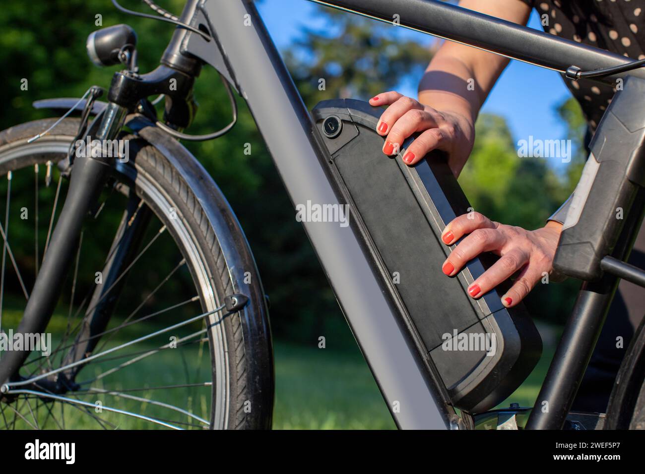 donna che tiene una batteria per bici elettrica montata sul telaio Foto Stock