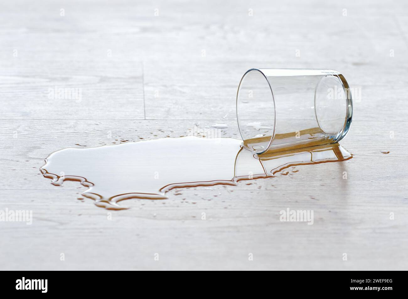 vetro d'acqua versato su pavimento di legno Foto Stock