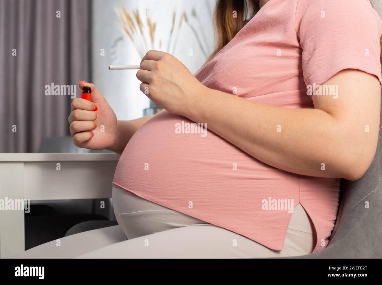 Una ragazza incinta con una grande pancia siede in cucina al tavolo e fuma. Fumo e gravidanza. Danno alla salute del bambino e della madre, tobac Foto Stock