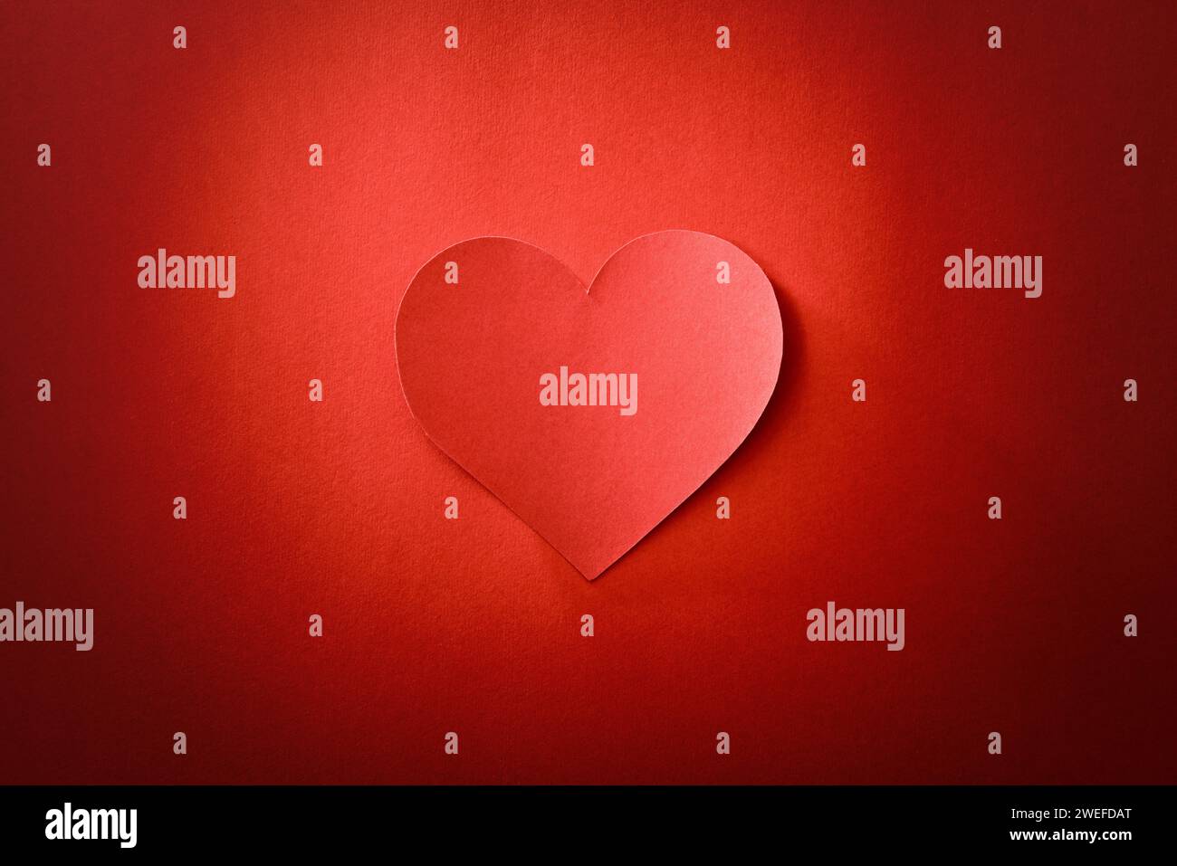Ritaglio del cuore al centro isolato su sfondo rosso testurizzato e gradiente. Vista dall'alto. Foto Stock