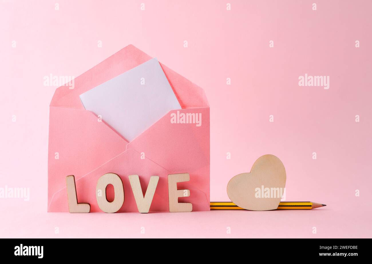 Busta rosa con lettere con amore di parola e cuore di legno con matita isolata su sfondo rosa. Vista frontale. Foto Stock