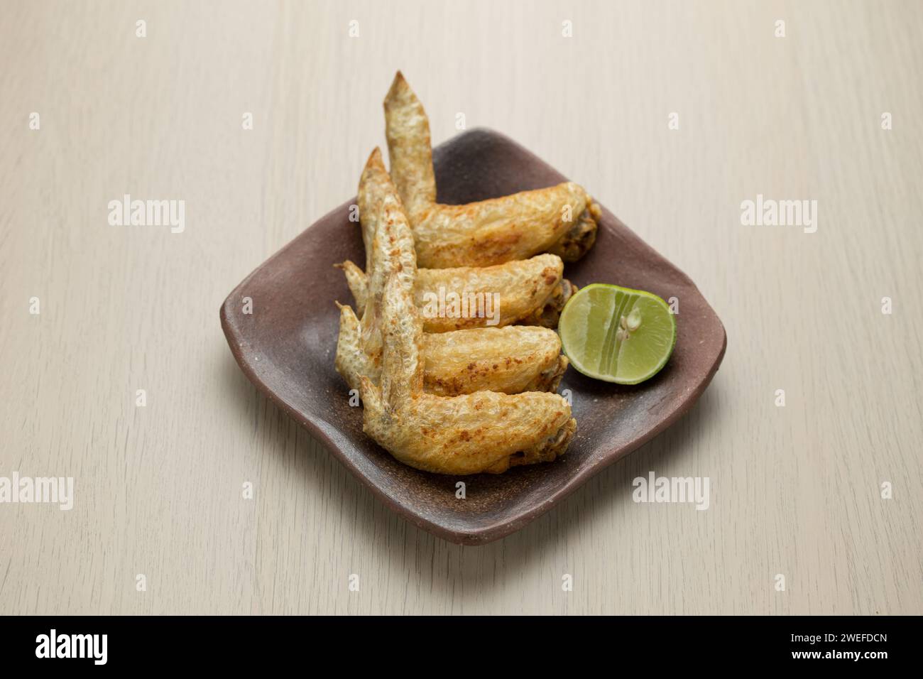 Ali di pollo fritte in stile thailandese su un piatto di ceramica marrone. Foto Stock