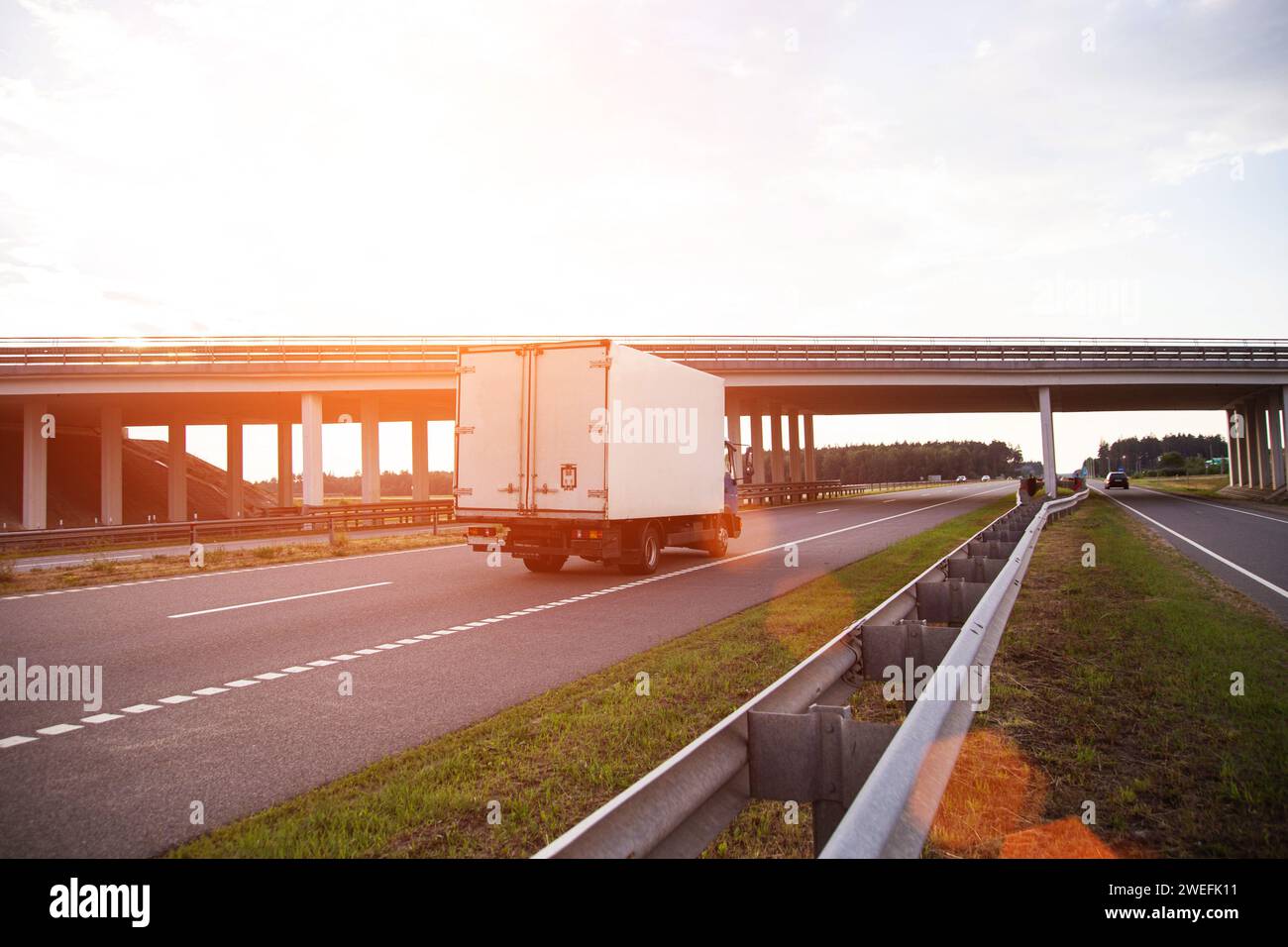 Un furgone commerciale refrigerato a basso tonnellaggio trasporta prodotti deperibili in estate su una strada di campagna sullo sfondo del tramonto. Industria Foto Stock