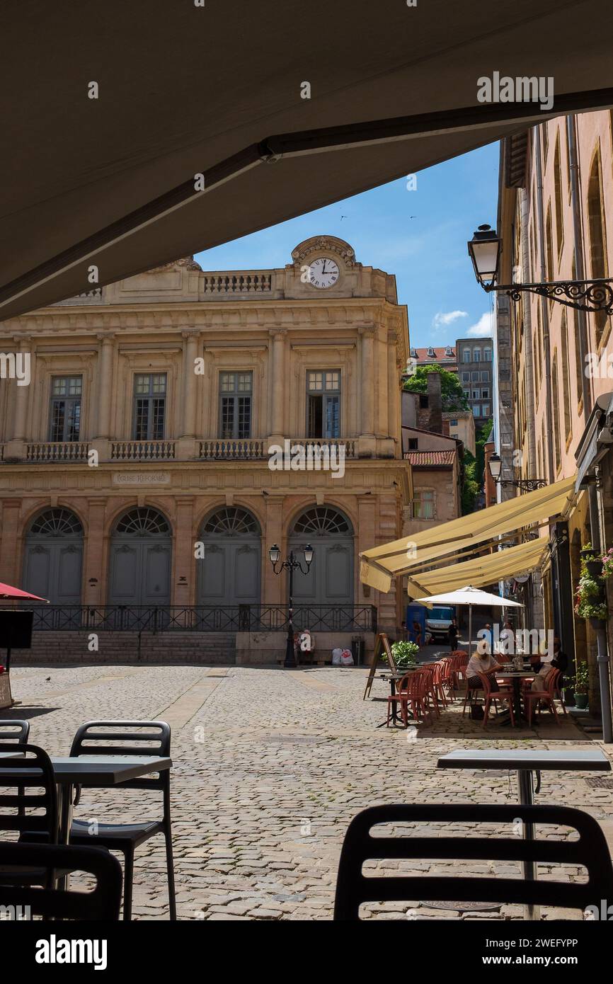 Lione, Francia, 2023. Turisti seduti nei caffè Place du Change, con il tempio protestante del cambiamento sullo sfondo (verticale) Foto Stock