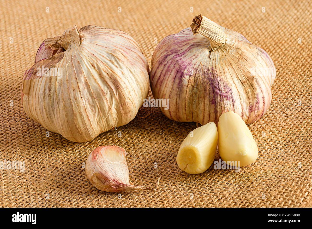 I bulbi all'aglio fresco e i chiodi di garofano disposti in modo ordinato su una tela rustica Foto Stock
