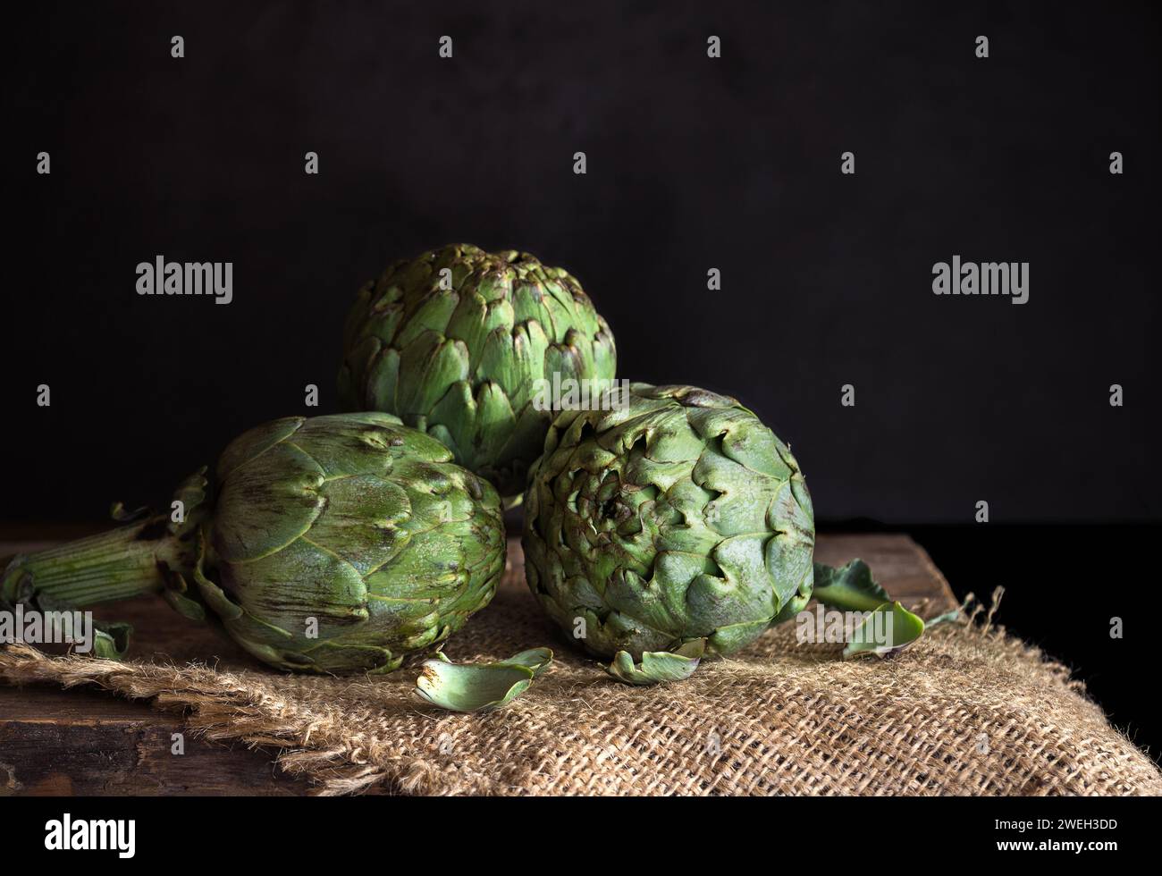 Cuori di carciofi freschi su tavola di lino - toni scuri e lunatici Foto Stock