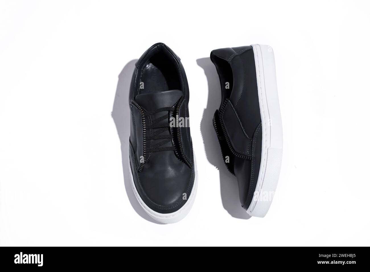 sneaker nere con vista dall'alto su sfondo bianco e ombre rigide. Scarpe da donna. Foto Stock
