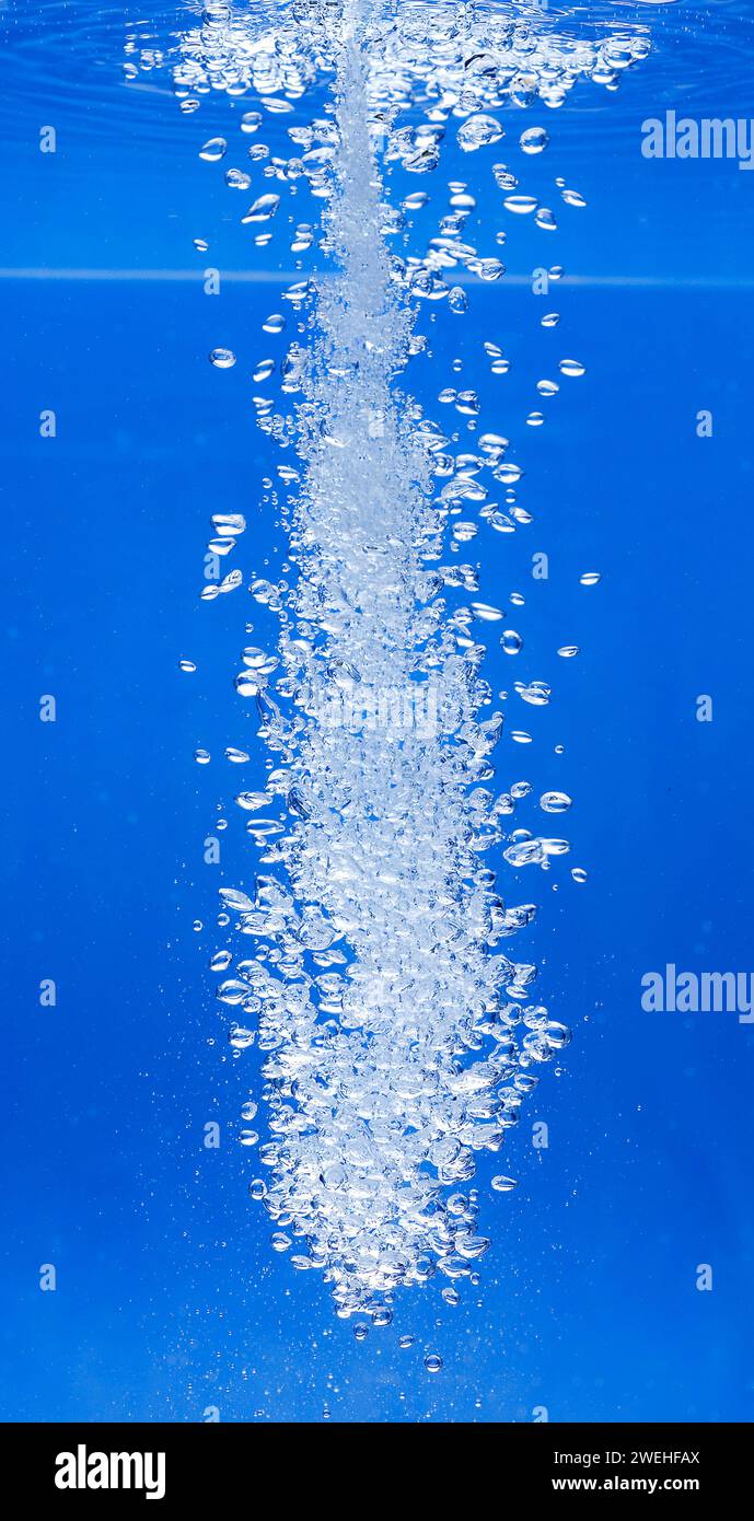 un sottile getto d'acqua penetra nella superficie dell'acqua e produce molte bolle d'aria nell'acqua blu di un acquario Foto Stock