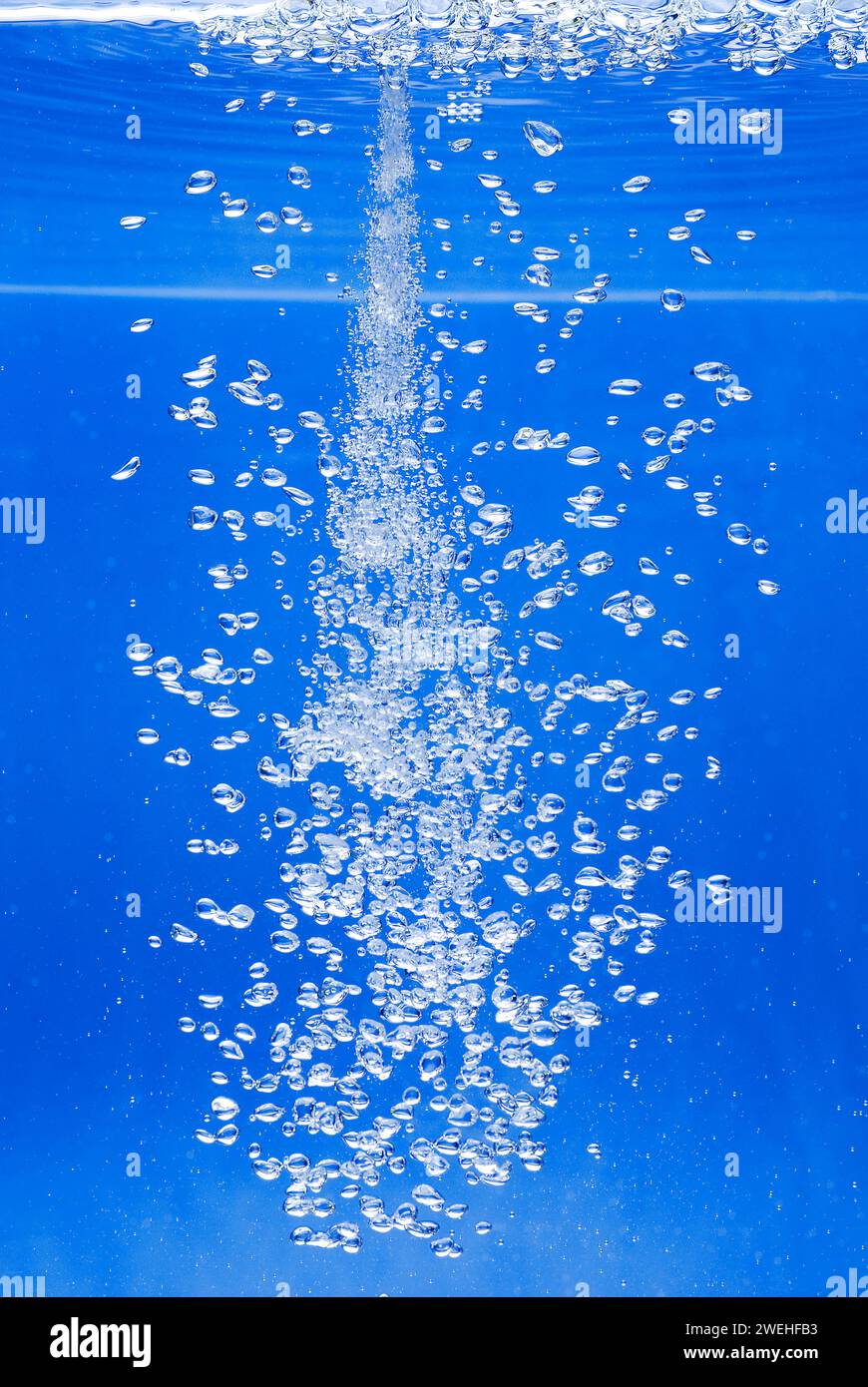 un sottile getto d'acqua penetra nella superficie dell'acqua e produce molte bolle d'aria nell'acqua blu di un acquario Foto Stock