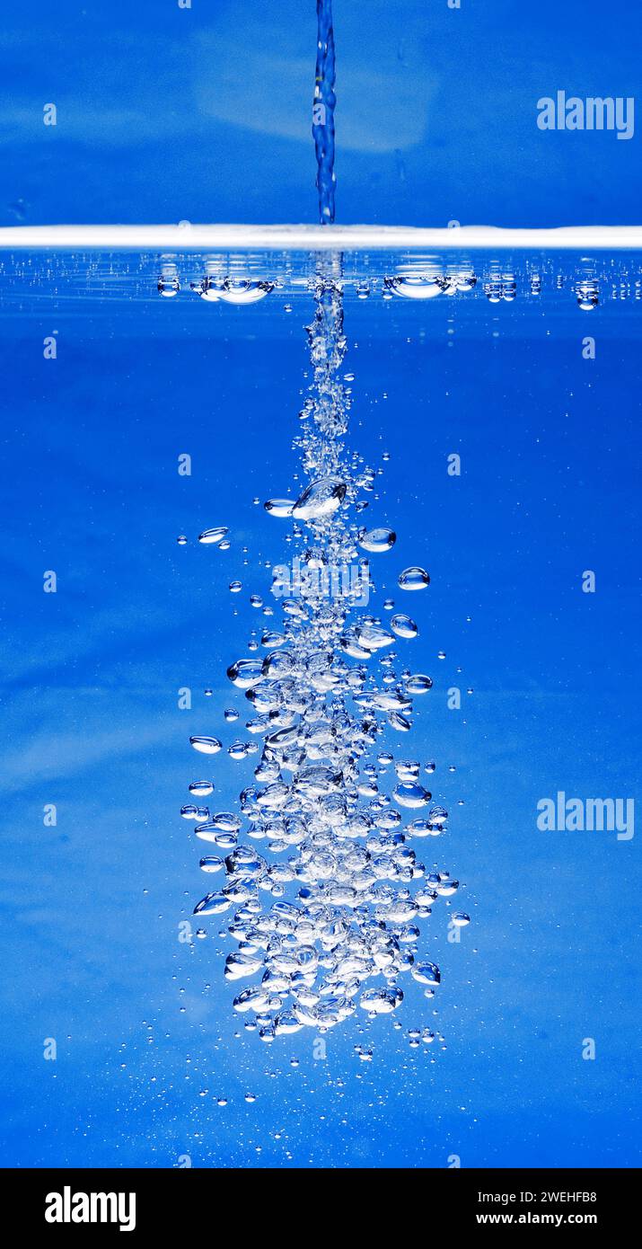 un sottile getto d'acqua penetra nella superficie dell'acqua e produce molte bolle d'aria nell'acqua blu di un acquario Foto Stock