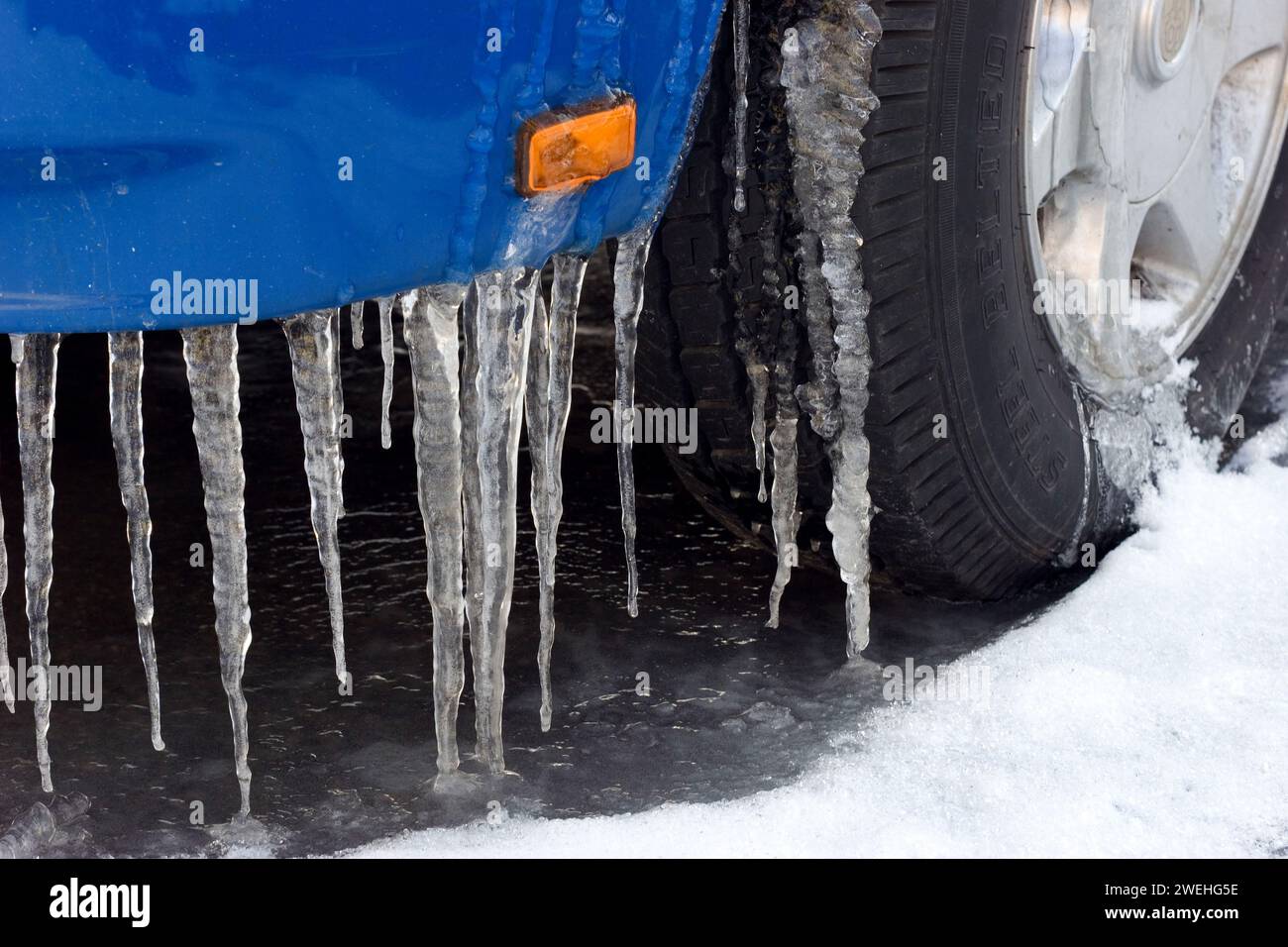 sono riconoscibili i lunghi ghiacci su un'auto blu, il simbolo della pioggia ghiacciata, i primi piani, il parafango e la ruota anteriore Foto Stock